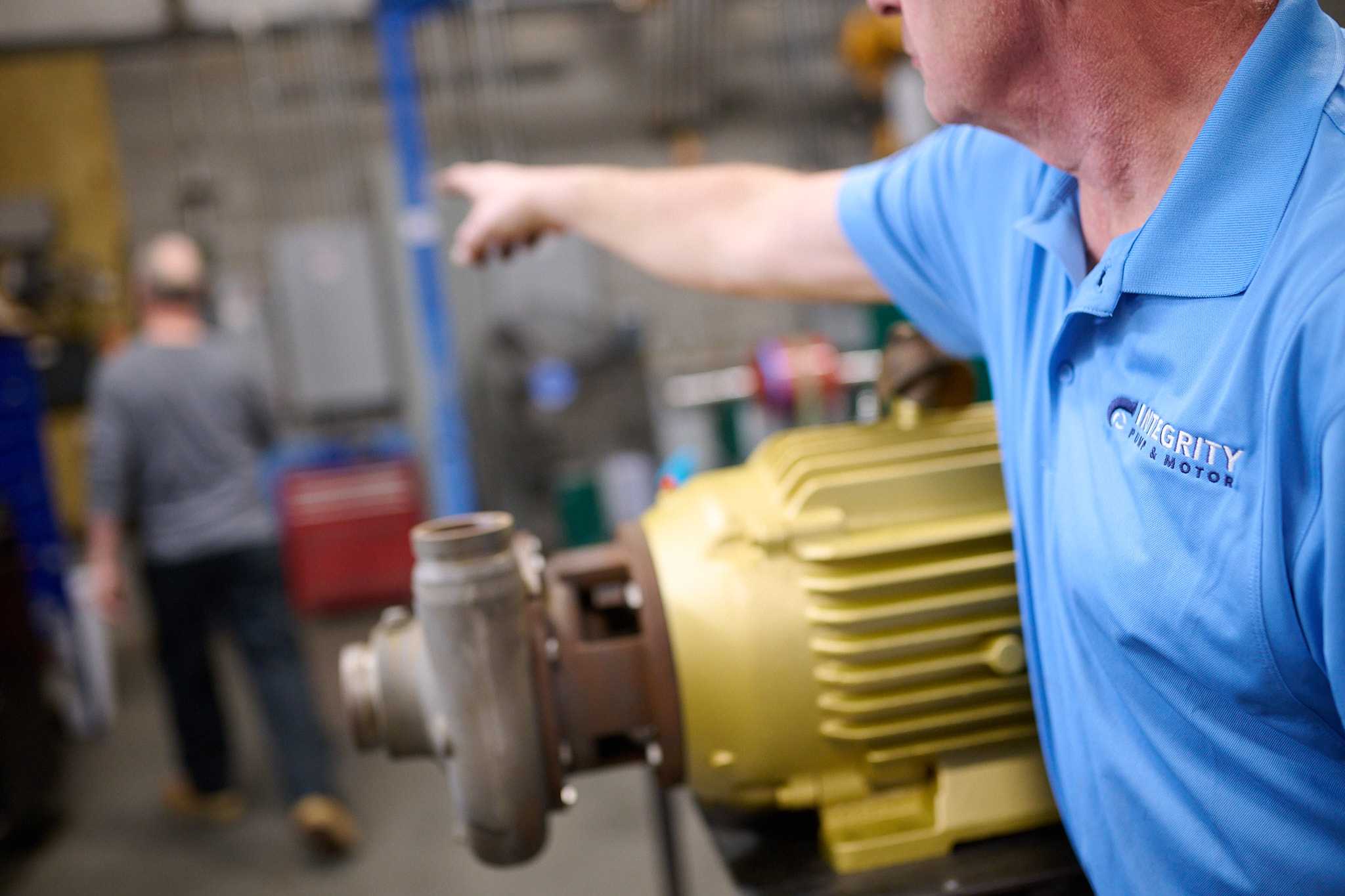 mployee of "Integrity Pump & Motor" pointing towards a large industrial pump or motor assembly